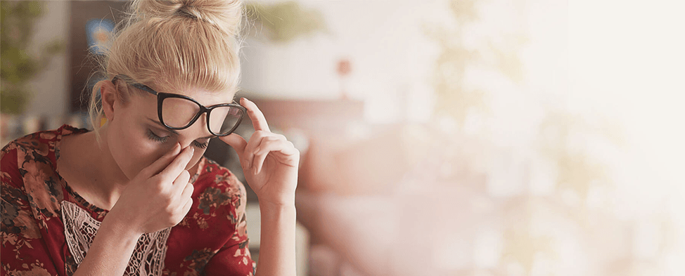A woman wearing glasses is rubbing her eyes.